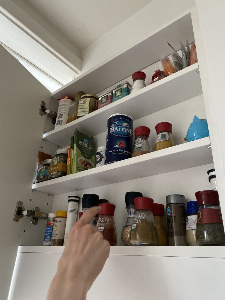 Person opening the spice cupboard, about to put back the paprika powder.