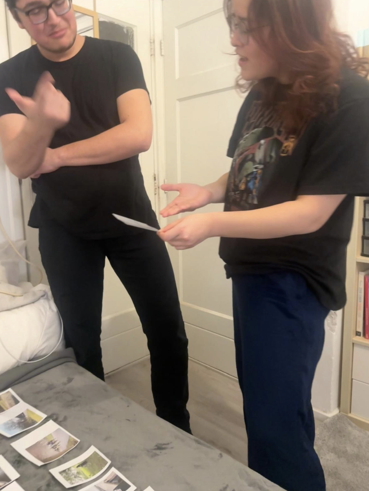 Two people standing at a surrounded by printed photographs, talking and pointing at images during a creative reflection session.